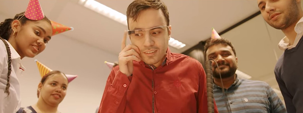 Envision Glasses(인비전 글래스)를 소개하는 이미지1. 파티 모자를 쓴 동료들에게 둘러싸인 채 스마트 안경을 착용한 남성의 모습을 보여줍니다.