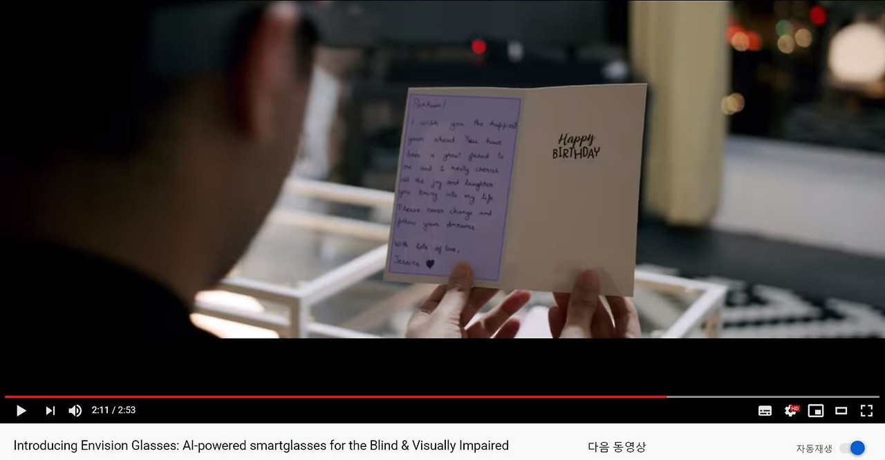 Envision Glasses(인비전 글래스)를 소개하는 이미지3. 안경을 쓴 사용자가 손으로 쓴 'Happy Birthday' 카드를 읽고 있습니다.