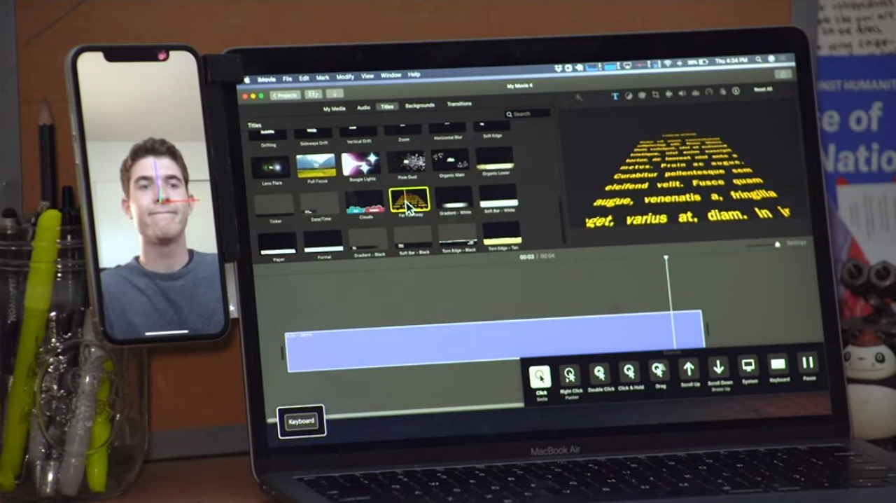 'Hawkeye Access for Mac'의 작동 시연 장면. 맥북 옆에 거치된 아이폰이 사용자의 얼굴(코에 빨간 점)을 추적하고, 그 머리 움직임을 이용해 맥북의 비디오 편집 소프트웨어 커서를 제어하는 모습을 보여줍니다.